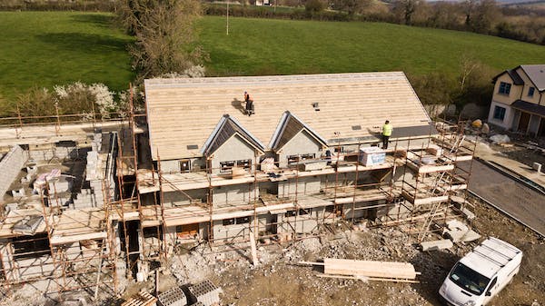 workers building custom home with white car nearby